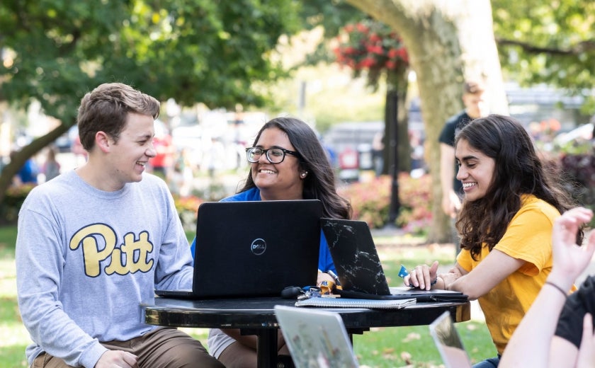 Students laughing next to computers outdoors